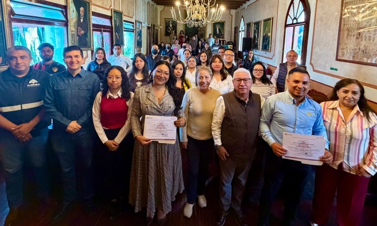 Grupo de personas en una ceremonia de reconocimiento en un salón elegante con pinturas y candelabros, celebrando logros y entregando certificados.