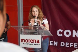 Mujer con cabello rizado y expresión entusiasta hablando en un podio durante un evento político en Tlaxcala, México.