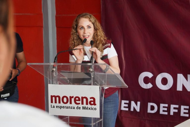 Mujer con cabello rizado y expresión entusiasta hablando en un podio durante un evento político en Tlaxcala, México.