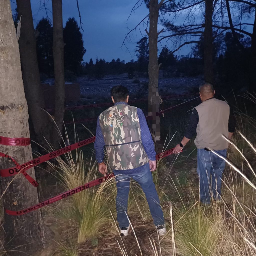 Dos hombres inspeccionan un área forestal cercada con cinta de advertencia en un entorno natural al atardecer.