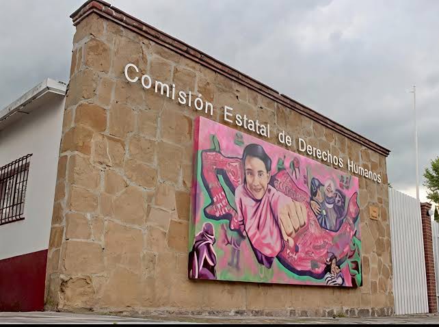 Fachada de la Comisión Estatal de Derechos Humanos en Tlaxcala con mural colorido y texto en la pared de piedra.