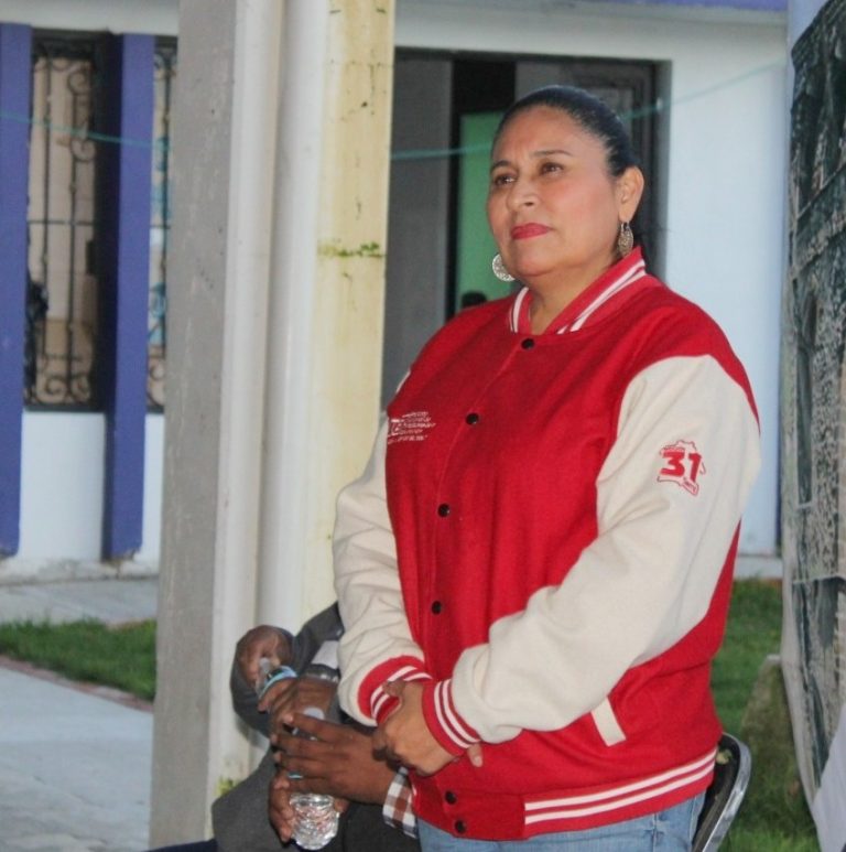 Mujer con chaqueta roja y blanca, de pie en un entorno urbano, mirando hacia la derecha con expresión pensativa.