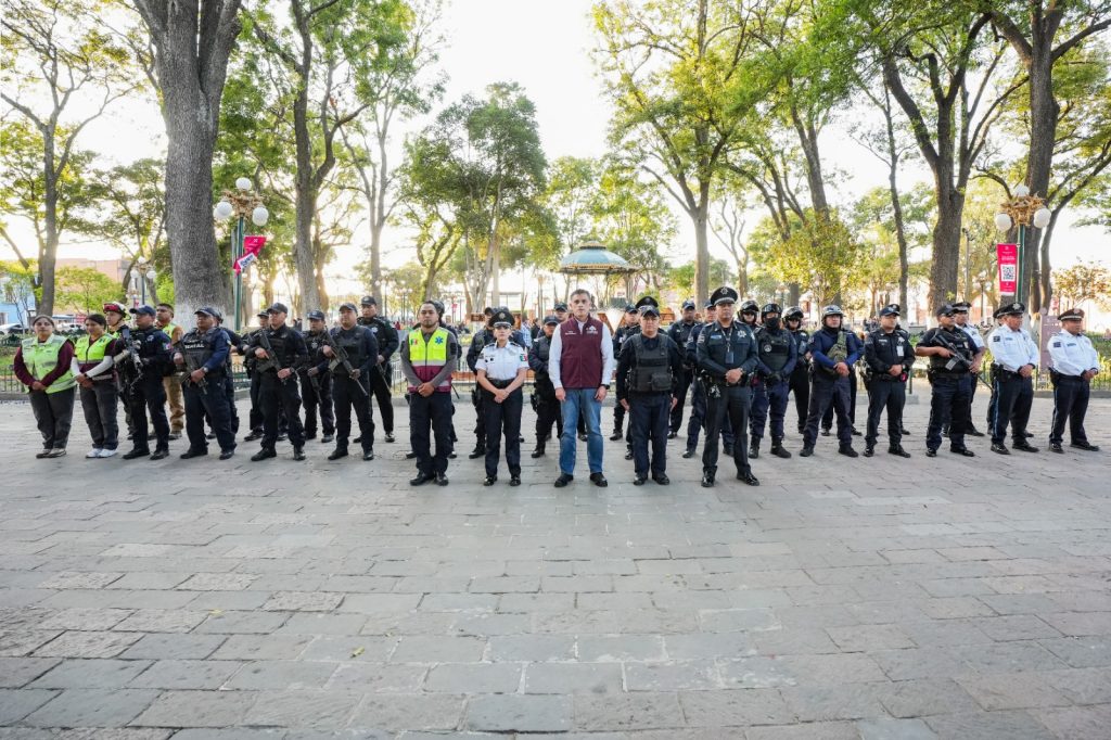 Grupo de policías y oficiales en una plaza pública con árboles y farolas, en una reunión o evento oficial en Tlaxcala, México.