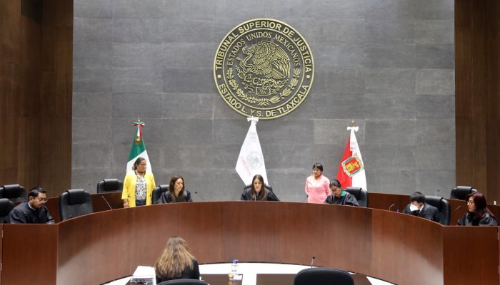 Sala de sesiones del Congreso de Tlaxcala con autoridades y banderas oficiales en un entorno formal y moderno.