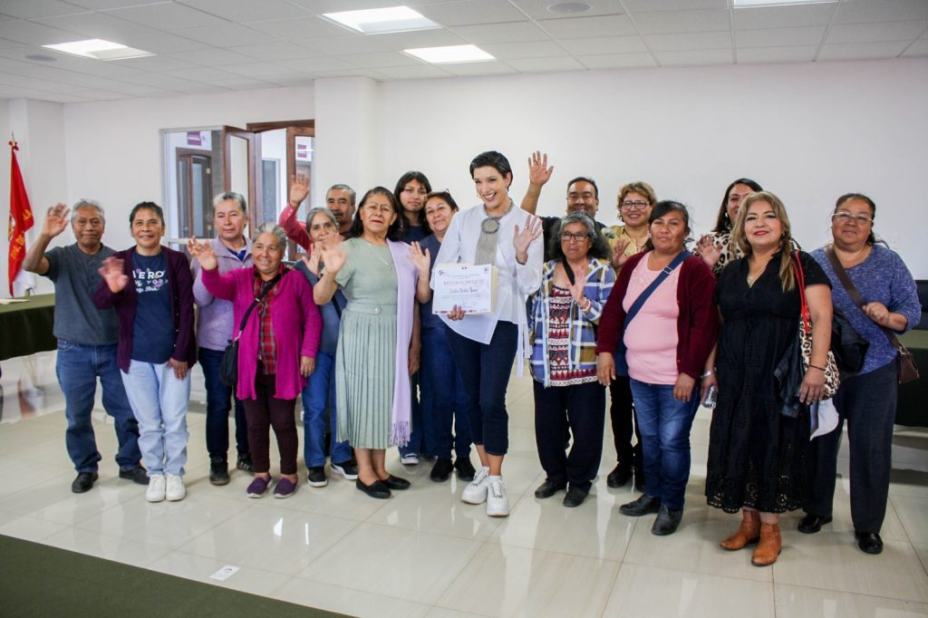 Una grupo diverso de personas en un espacio interior, celebrando y sonriendo, con algunos levantando las manos en señal de saludo o victoria, en un ambiente de camaradería y alegría.