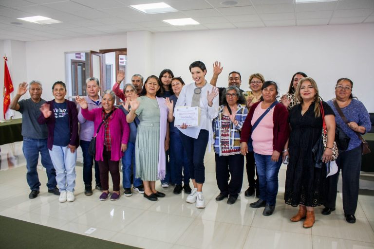 Una grupo diverso de personas en un espacio interior, celebrando y sonriendo, con algunos levantando las manos en señal de saludo o victoria, en un ambiente de camaradería y alegría.