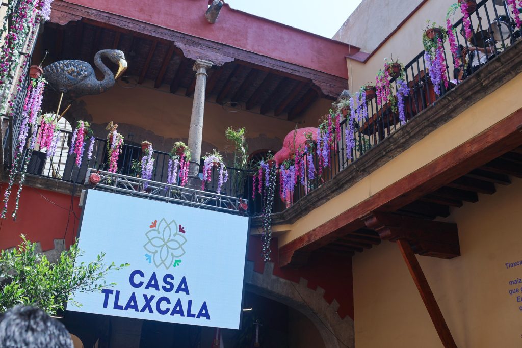 Fachada de Casa Tlaxcala decorada con flores en un patio interior, con un cartel que indica el nombre del lugar.