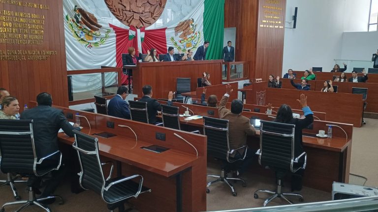 Reunión oficial en el Congreso de Tlaxcala con legisladores y funcionarios durante una sesión parlamentaria, con la bandera de México y el escudo nacional en el fondo.