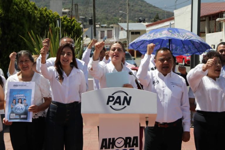 Grupo de mujeres y hombre en una manifestación política, sosteniendo pancartas y levantando el puño en señal de protesta, en una calle de Tlaxcala, México.