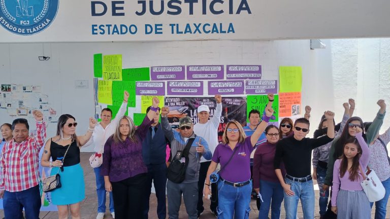 Manifestantes en una protesta pacífica frente a una oficina de justicia en Tlaxcala, sosteniendo carteles y levantando los puños en señal de resistencia y demanda de justicia.