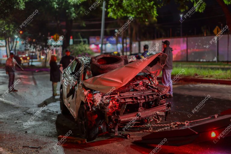Vehículo accidentado con daños severos en la parte frontal tras un choque en la calle, con presencia de personas y luces de emergencia en Tlaxcala, México.