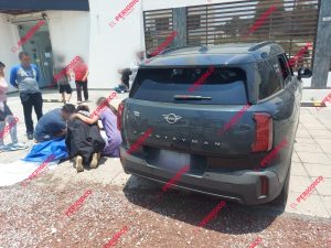 ACCIDENTE DE TRÁFICO CON VEHÍCULO SUV NEGRO Y PERSONAS ATENDIENDO LA ESCENA, EN EL EXTERIOR DE UN EDIFICIO MODERNO EN TLAXCALA, MÉXICO, CON VARIAS PERSONAS OBSERVANDO Y UNA VÍCTIMA RECIBIENDO ASISTENC.