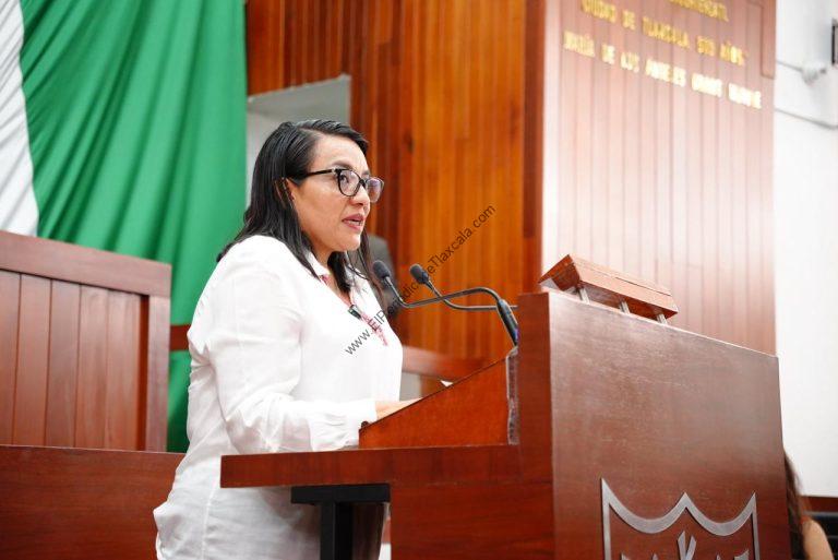 Mujer hablando en un podio durante una conferencia en un entorno formal con fondo de cortinas verdes y madera.