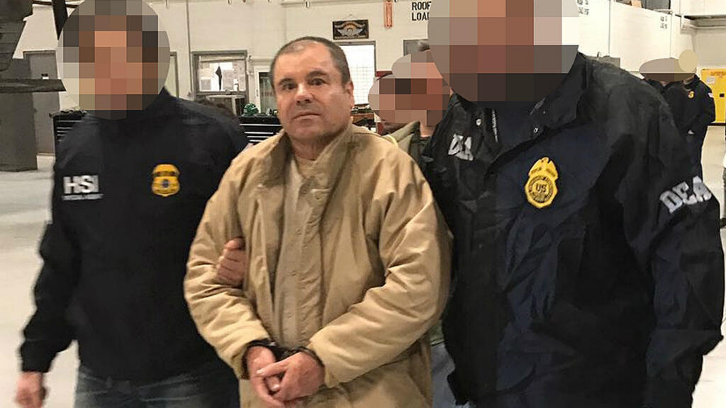Hombre detenido por autoridades policiales en un aeropuerto, rodeado de agentes con uniformes negros y distintivos de la policía.