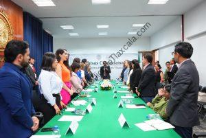 Personas en una reunión formal en una sala de conferencias, participando en un evento oficial en Tlaxcala, México, con una mesa larga y asistentes de pie en ambos lados.