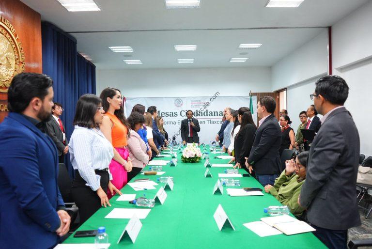 Personas en una reunión formal en una sala de conferencias, participando en un evento oficial en Tlaxcala, México, con una mesa larga y asistentes de pie en ambos lados.
