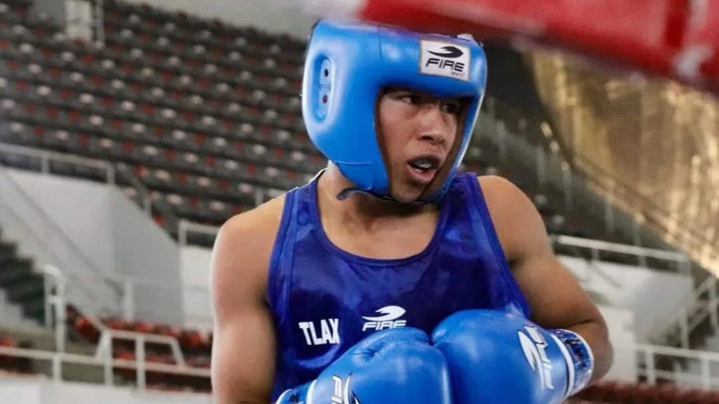 Atleta de boxeo en entrenamiento con casco azul y guantes, concentrado en su combate en un ring de boxeo, con gradas vacías en el fondo.