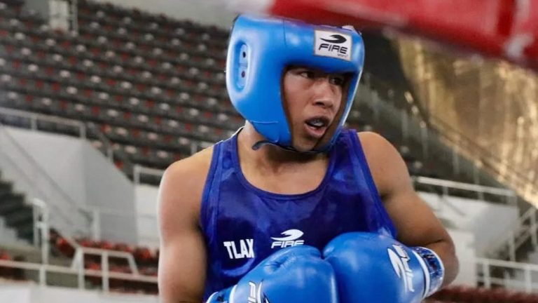 Atleta de boxeo en entrenamiento con casco azul y guantes, concentrado en su combate en un ring de boxeo, con gradas vacías en el fondo.