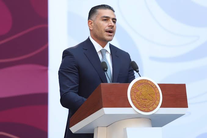 Hombre en traje oscuro hablando en un podio con el escudo de México, en un evento oficial.