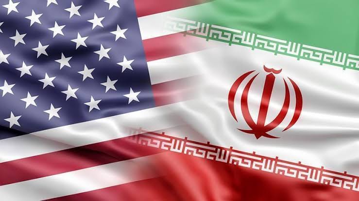 Banderas de Estados Unidos e Irán onde ondean juntas, simbolizando la relación diplomática entre ambos países. La imagen muestra las banderas en un fondo que refleja movimiento y tensión polític.